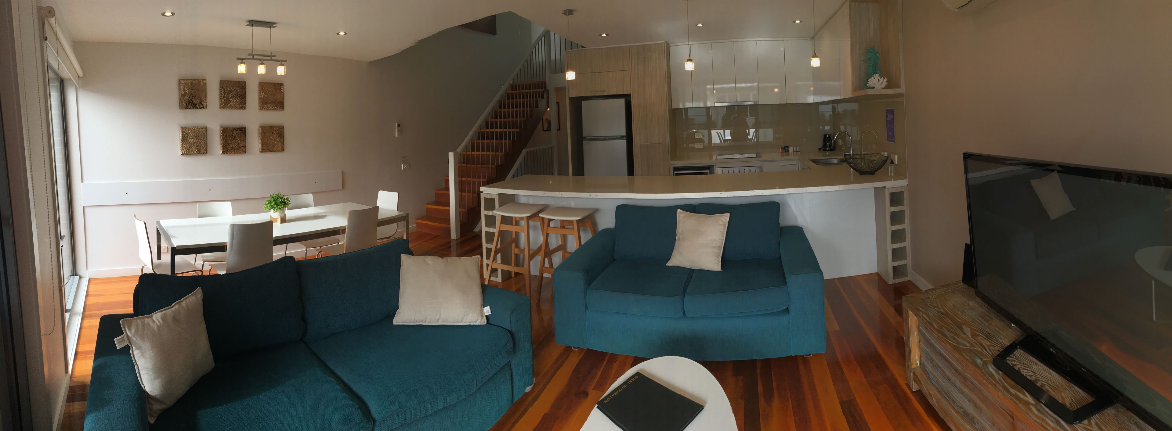A modern living room with a sofa, a TV, and a kitchen area with a dining table.
