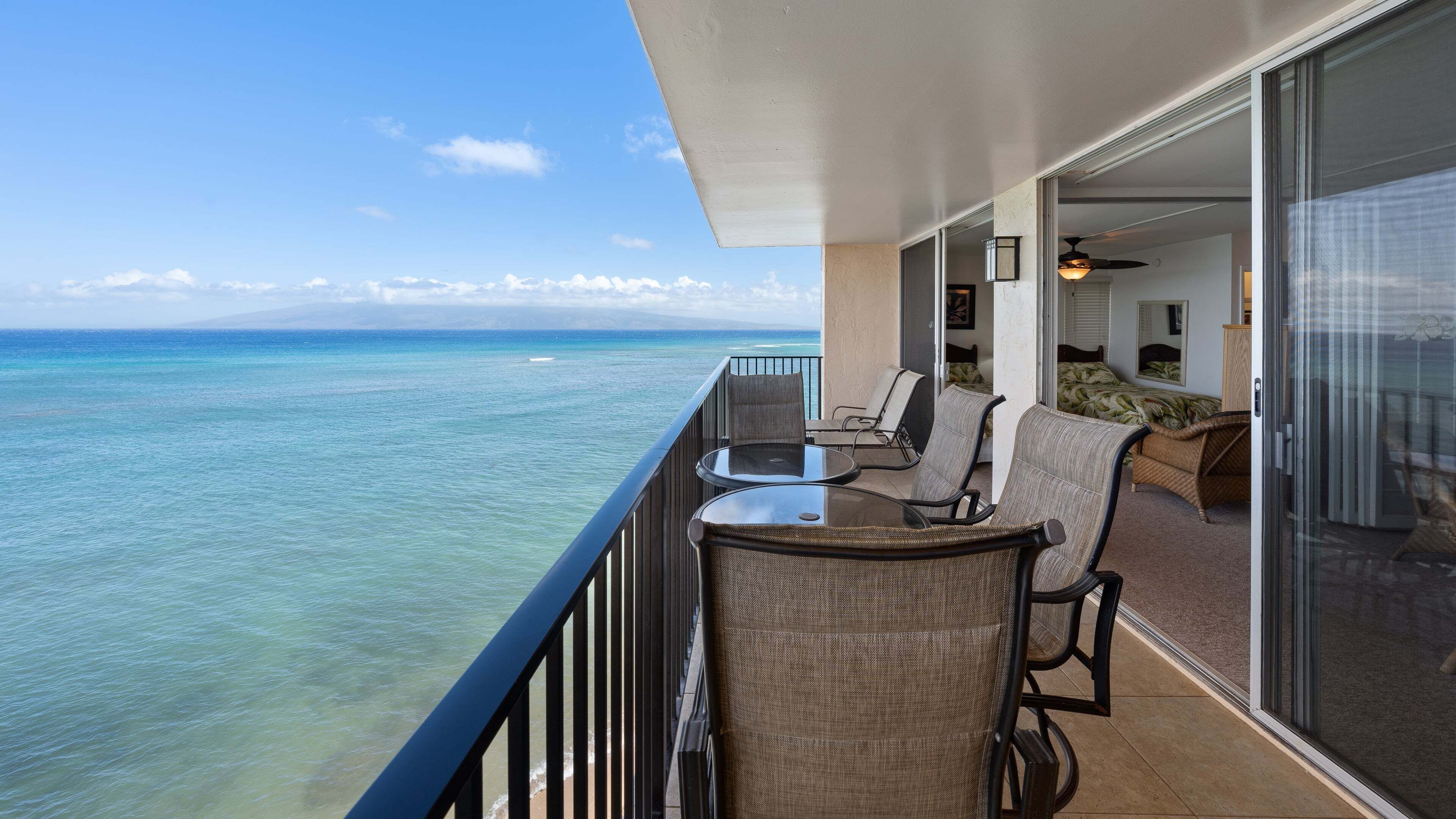 A balcony with a glass door leading to a room, overlooking a clear ocean view.