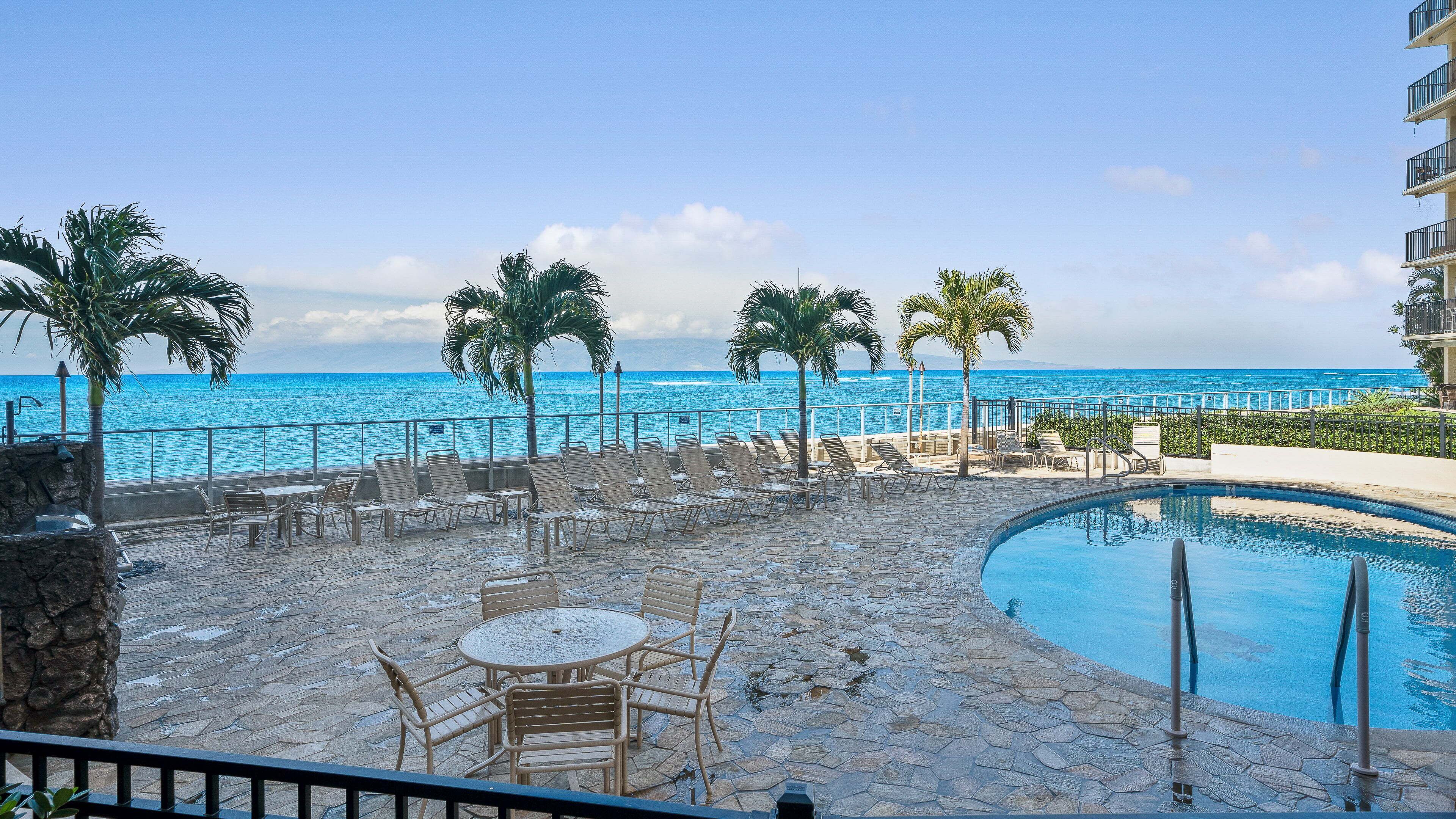 Zona de piscina con sillones reclinables y una mesa, con vistas al mar azul y despejado.