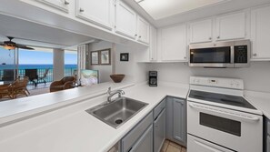 Eine moderne Küche mit weißen Schränken, einer Edelstahl-Spüle, einer eingebauten Mikrowelle und einem Backofen mit zwei Garstufen.