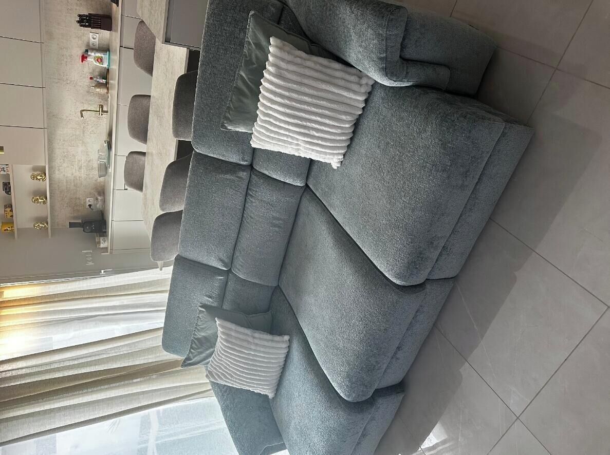 Un sofá gris con varios cojines y una cocina moderna al fondo.