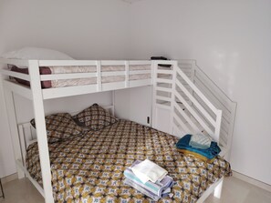 Ein Stockbett mit gemustertem Bettbezug und Kissen, einer weißen Geländer und einem zusammengefalteten Handtuch auf der unteren Etage.