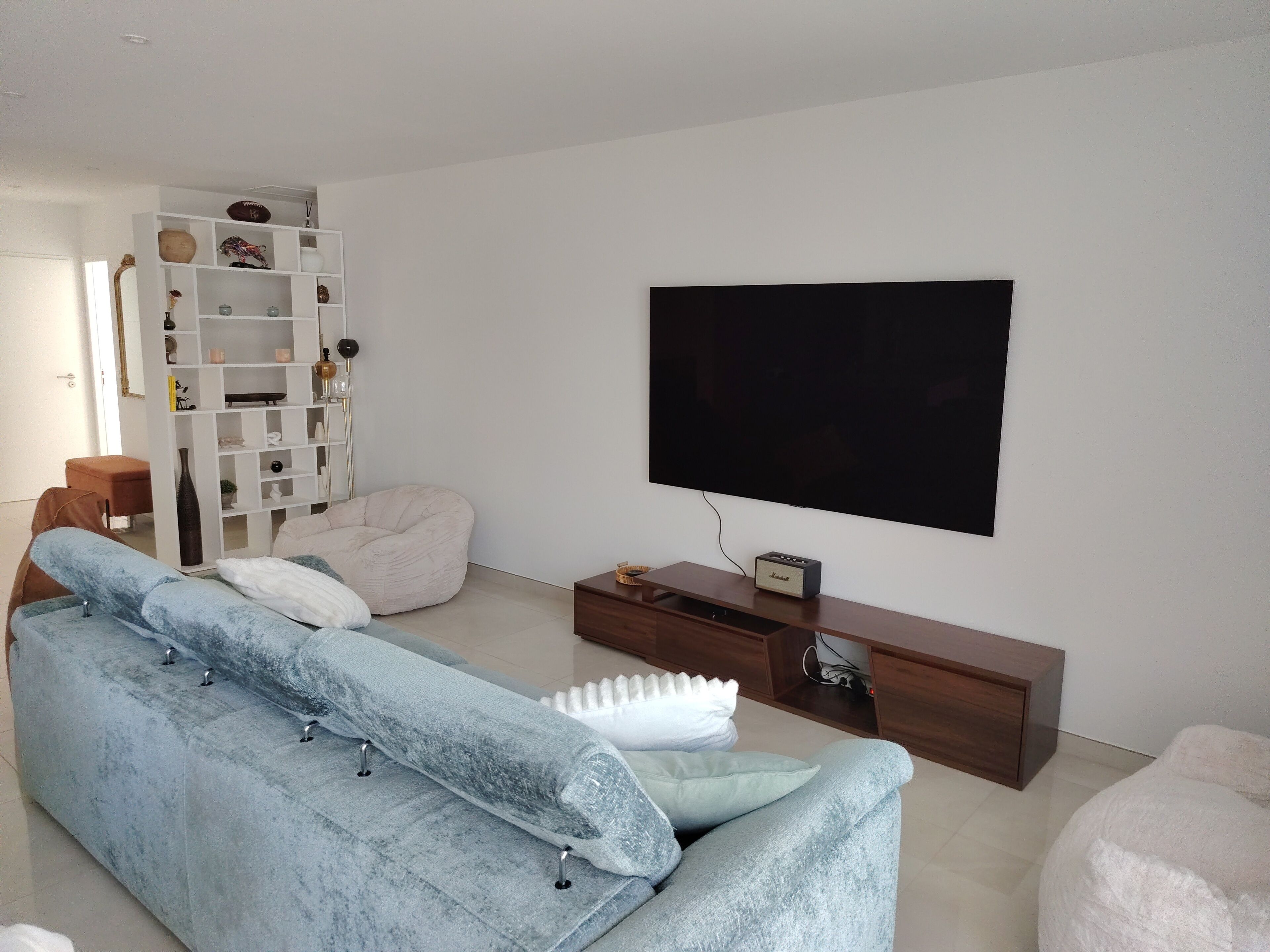 Een moderne woonkamer met een lichtblauwe bank, een witte pluchen zitzak, een flatscreen televisie en een houten tv-meubel.