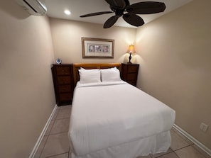 A bedroom with a bed, a nightstand, a wall-mounted lamp, a ceiling fan, and a framed picture on the wall. - Spacious Ground-Floor 2BR with AC & Garden Views, Walk to Beach- Maui Kamaole F107 (Kihei)