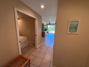 A hallway with a door leading to a bathroom, a small table, and a sign on the wall. - Spacious Ground-Floor 2BR with AC & Garden Views, Walk to Beach- Maui Kamaole F107 (Kihei)