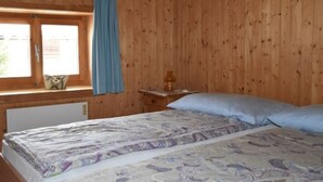 Quarto de madeira com cama, janela com cortinas e mesa de cabeceira com abajur.