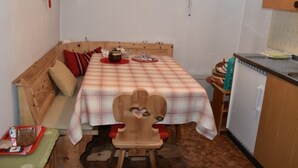 Quarto pequeno e acolhedor com um banco de madeira, uma mesa com toalha xadrez e uma pequena cozinha compacta.