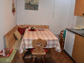 Una habitación pequeña y acogedora con un banco de madera, una mesa con mantel a cuadros y una kitchenette.
