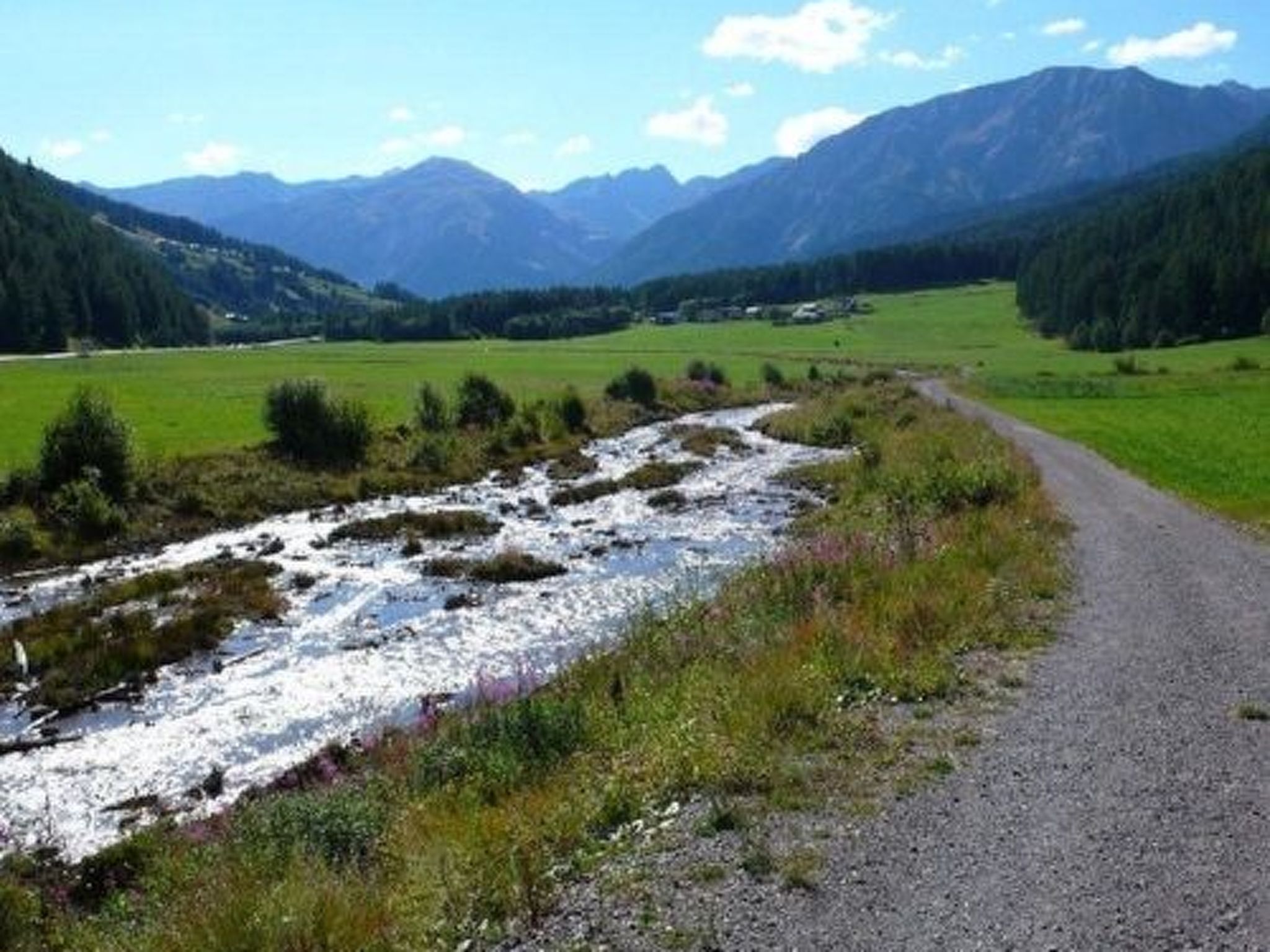 A gravel path alongside a river with mountains in the background.
