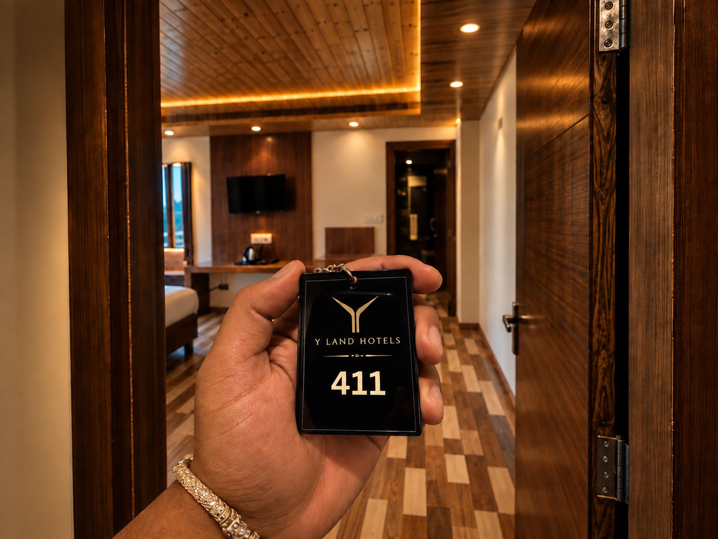 Egy kéz, amelyben egy fekete színű kulcstartó van, rajta a „Y LAND HOTELS” felirattal és a „411” számmal.