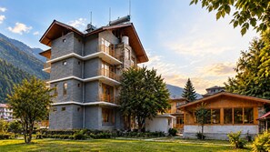 Un edificio de varios pisos con balcones, rodeado de vegetación y montañas.