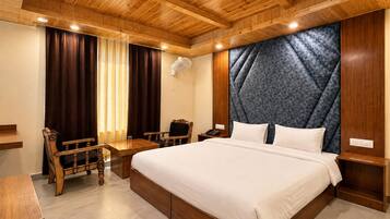 Una camera d'albergo con soffitto in legno, un letto grande con lenzuola bianche, un comodino in legno, una sedia di legno e una scrivania con una poltrona.
