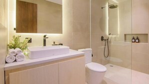 Et moderne badeværelse med et stort spejl, en hvid vask, et toilet og et bruseområde med glasvægge.