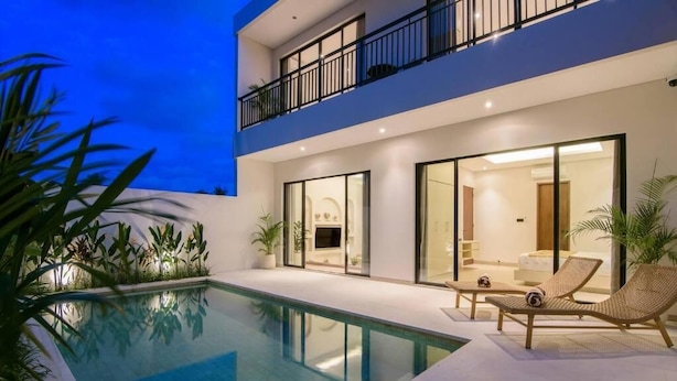 Et moderne hus med to etager, swimmingpool, udendørs siddepladser og store vinduer.