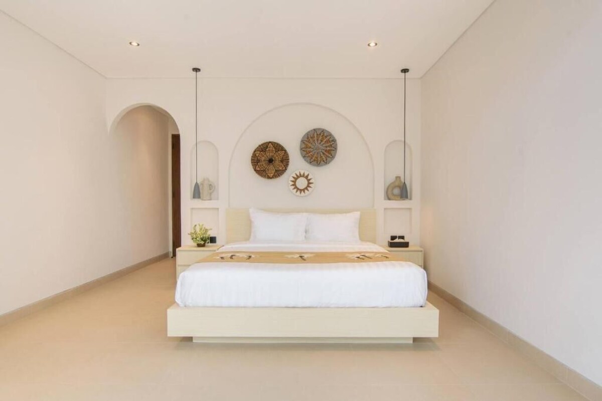 Un dormitorio minimalista con una cama centrada, flanqueada por mesitas de noche con lámparas.