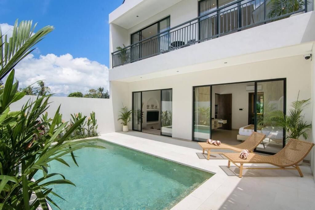 Una casa moderna de dos pisos con piscina, sillas de descanso y un balcón.
