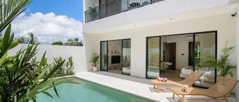 A modern two-story house with a swimming pool, lounge chairs, and a balcony.