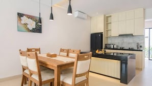 Et moderne køkken med en central ø, et træspisebord med stole og hængende lamper.