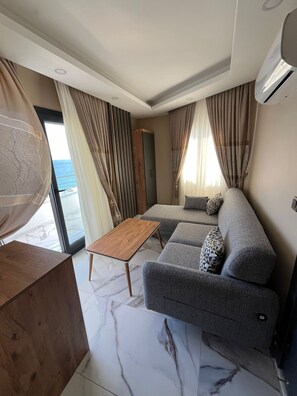 A modern living room with a sofa, a wooden coffee table, and a view of the sea. - Korasion Otel (Mersin)