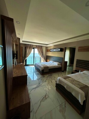 A hotel room with a large bed, a desk, and a view of the sea. - Korasion Otel (Mersin)