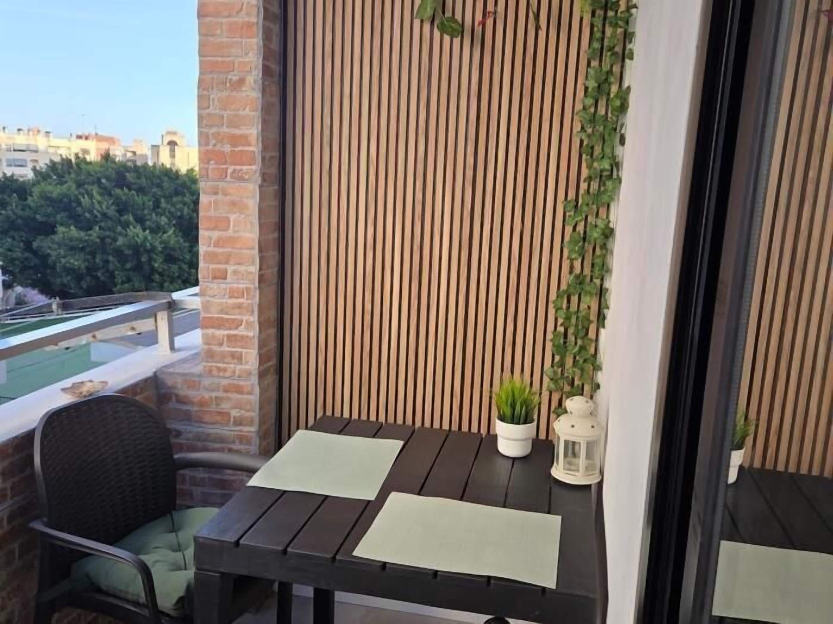A balcony with a wooden table and chairs, a potted plant, and a lantern.