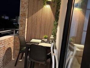 Un balcon avec une table et des chaises, un pot de fleurs et une vue sur la ville la nuit.