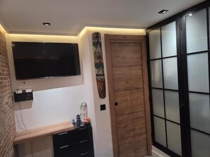 A room with a flat-screen TV mounted on the wall, a wooden door with frosted glass panels, and a black cabinet with drawers. - One-Bedroom Apartment with Terrace, AC and Lift in Central Torremolinos (Torremolinos)