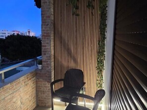 Ein Balkon mit einem Stuhl, einer Holzlamellenwand und Blick auf Gebäude im Hintergrund.