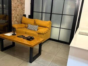 Ein Zimmer mit einer Couch, einem Holztisch und einer Ziegelwand.