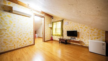 A room with a wooden floor, a television, a small table, and a refrigerator.