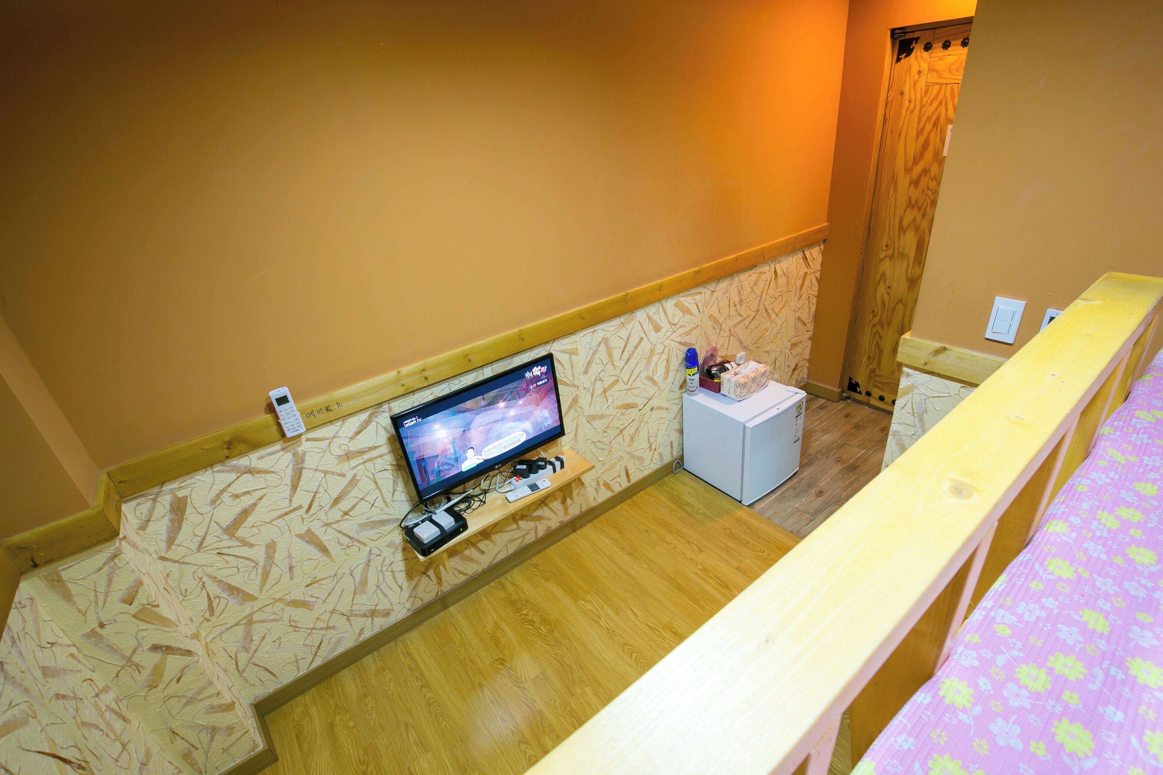 Una habitación de hotel con un televisor montado en la pared, una pequeña mesa blanca y un banco de madera.