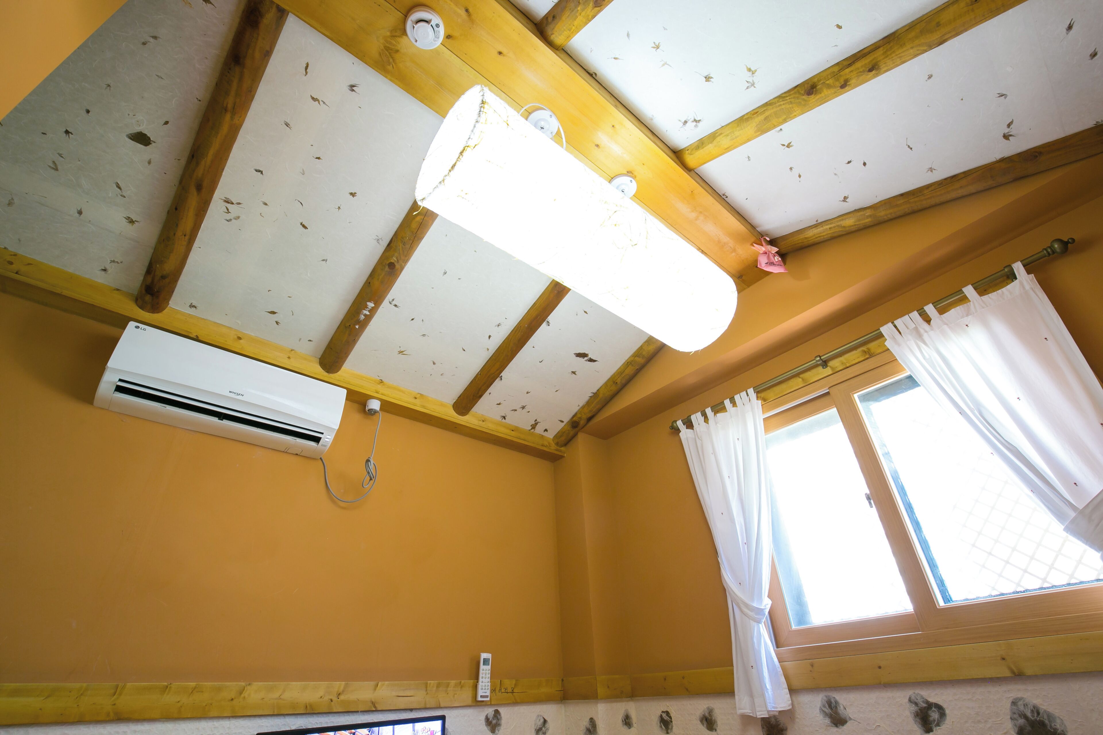 Una habitación con techo inclinado, un equipo de aire acondicionado, una ventana con cortinas y un termostato instalado en la pared.