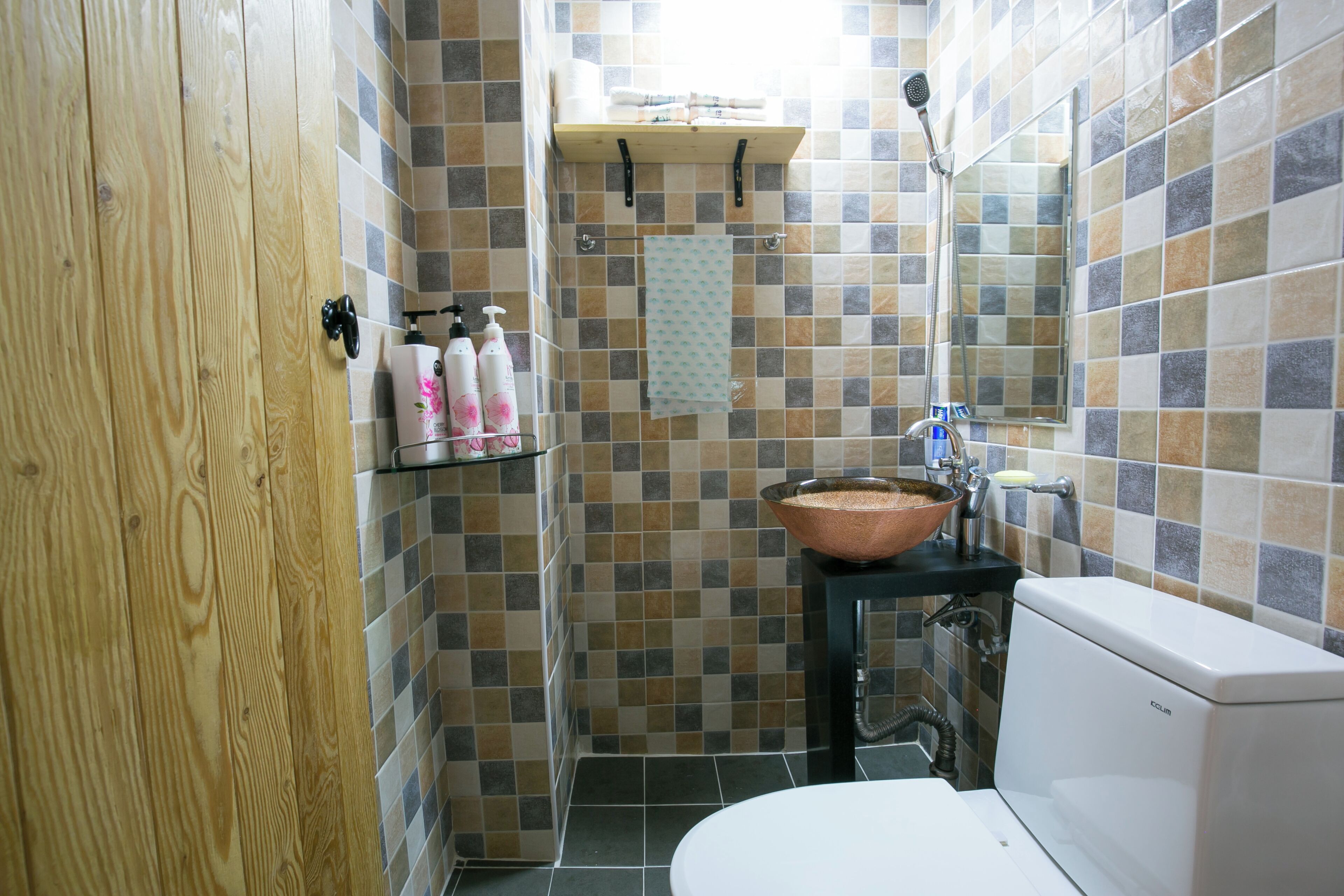 Un baño con puerta de madera, un lavabo con cuenca de cobre, inodoro y ducha con cabezal de ducha manual.