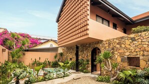 A modern building with a unique brick facade, a stone wall, and a variety of tropical plants.