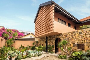 Un edifici modern amb una façana de maó singular, una paret de pedra i una varietat de plantes tropicals.