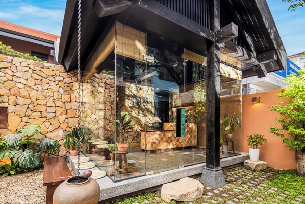 A modern building with a stone wall, a glass entrance, and a small garden with potted plants.