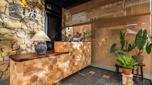 A reception area with a stone wall, a wooden reception desk, a lamp, and potted plants.