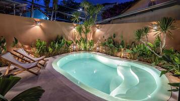 A swimming pool with a curved edge, surrounded by various plants and a few lounge chairs.