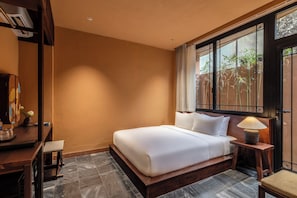 A hotel room with a large bed, a desk, and a window with a view of greenery.