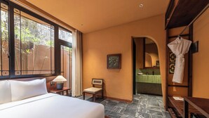 A hotel room with a bed, a chair, a desk, and a bathroom visible through an archway.