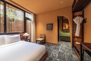 Habitació d'hotel amb un llit, una cadira, un escriptori i un bany visible a través d'una arcada.