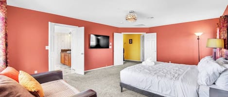 Ein Schlafzimmer mit einem Bett, einem Sessel, einem Fernseher und einer Tür zu einem Badezimmer.