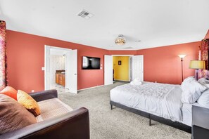 Un dormitorio con cama, una silla, un televisor y una puerta que da a un baño.