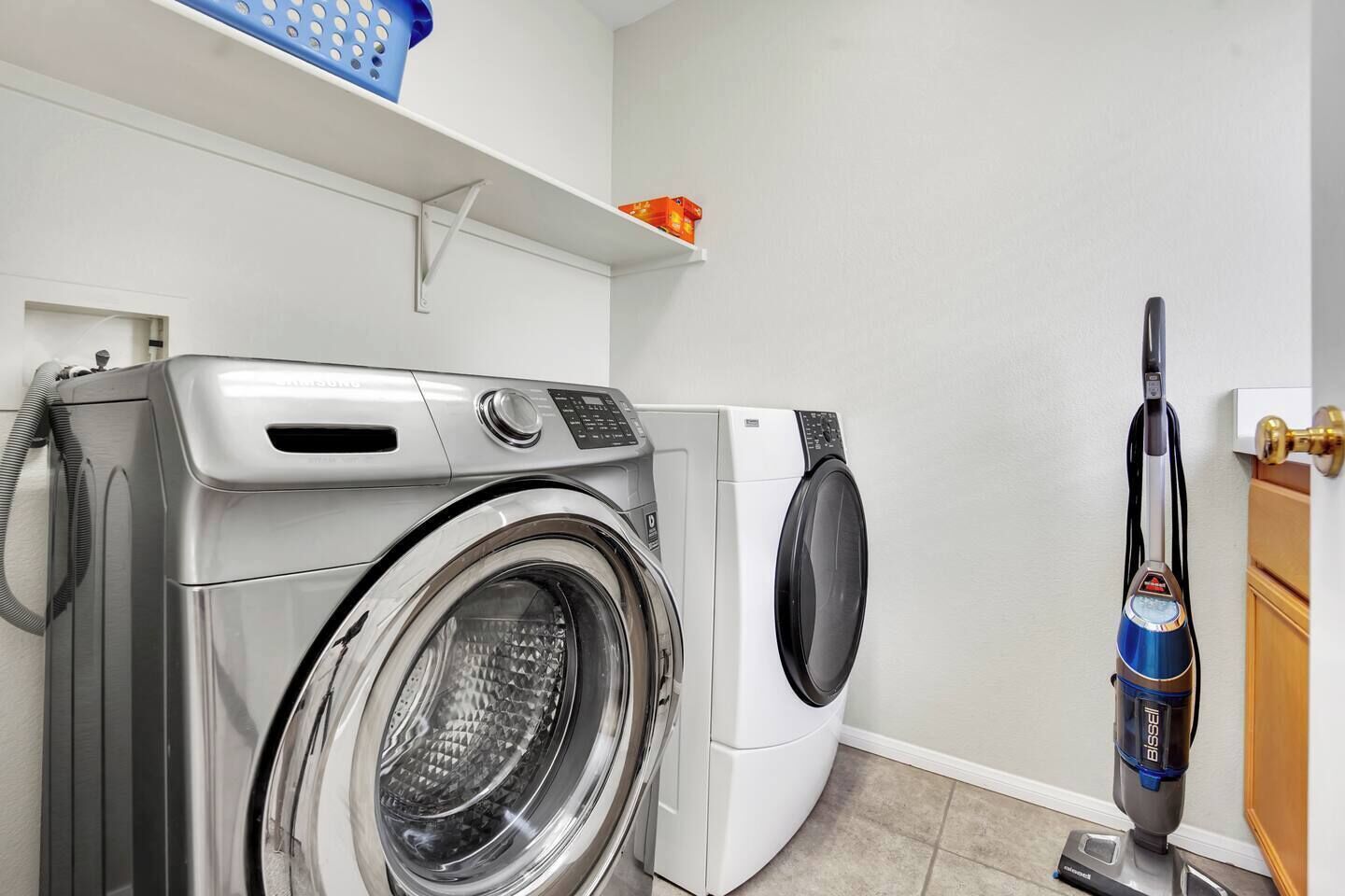 Een wasruimte met een wasmachine met voorlader en een stofzuiger.