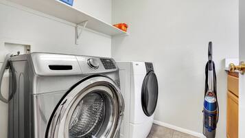 Een wasruimte met een wasmachine met voorlader en een stofzuiger.