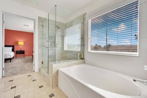 Un baño moderno con ducha de vidrio, una bañera amplia y una ventana con persianas.