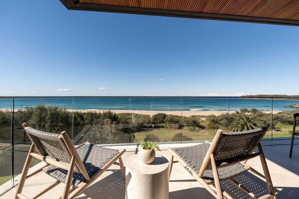 Un balcón con dos sillas y una mesa pequeña, con vista a una playa y al océano.