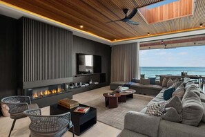 A modern living room with a fireplace, a large sofa, and a view of the ocean.