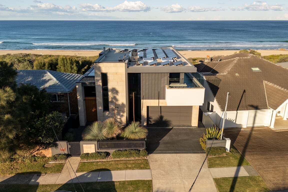 A modern house with a flat roof, a large window, and a view of the ocean.