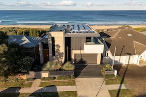 A modern house with a flat roof, a large window, and a view of the ocean.